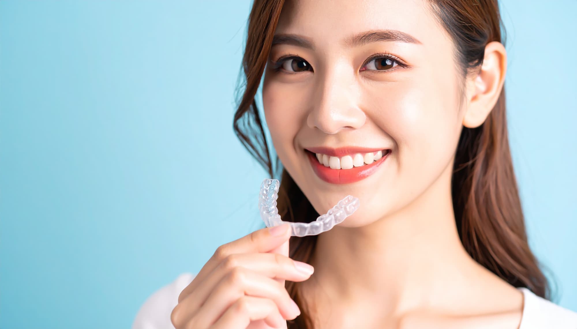 インビザラインのマウスピースを手に微笑んでいる受け口が治った女性
