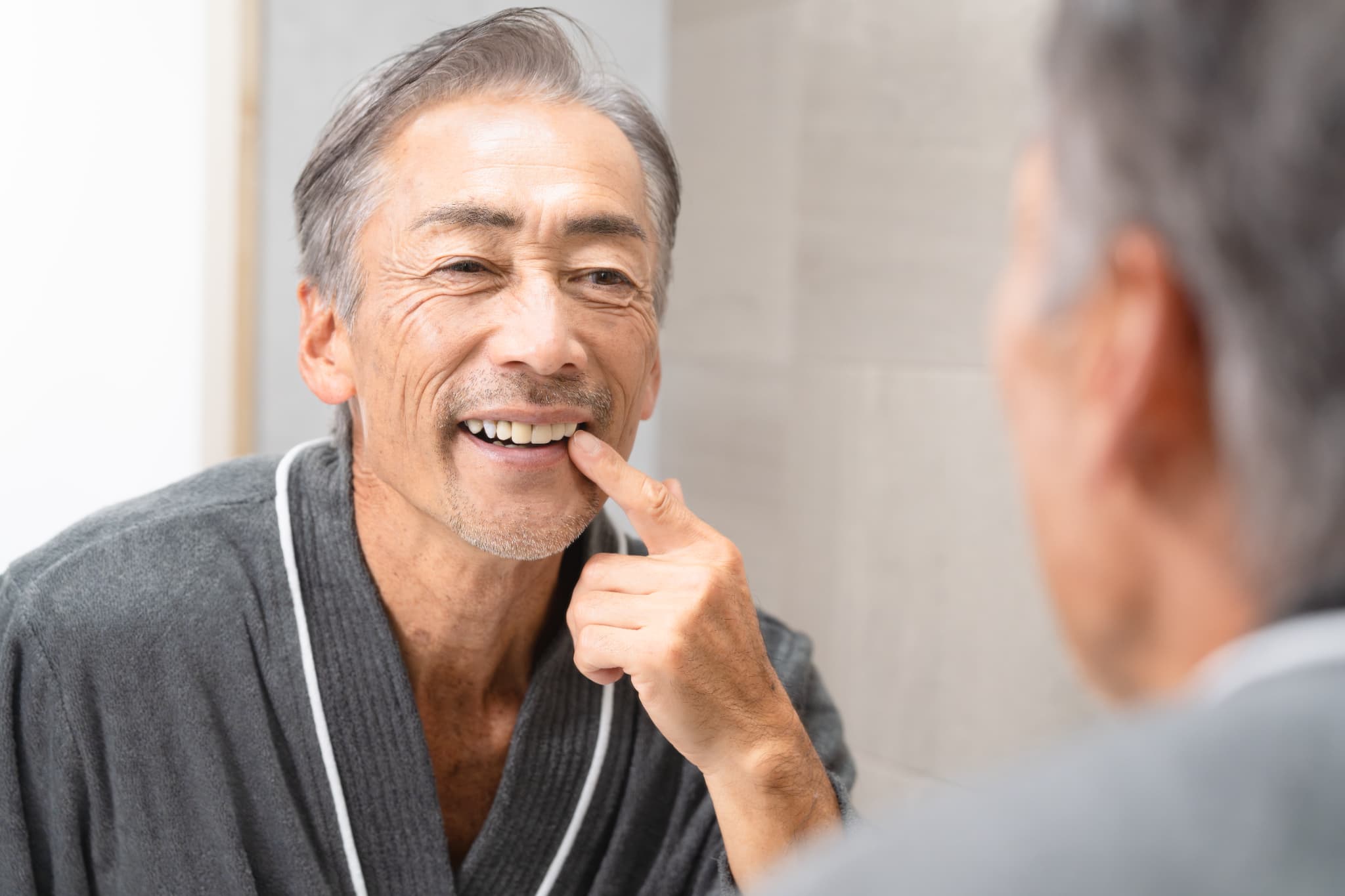 装着した入れ歯の自然な見た目を鏡で確認して満足している男性