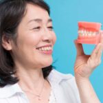 入れ歯の模型を手に持った笑顔の女性