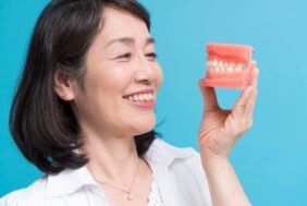 入れ歯の模型を手に持った笑顔の女性