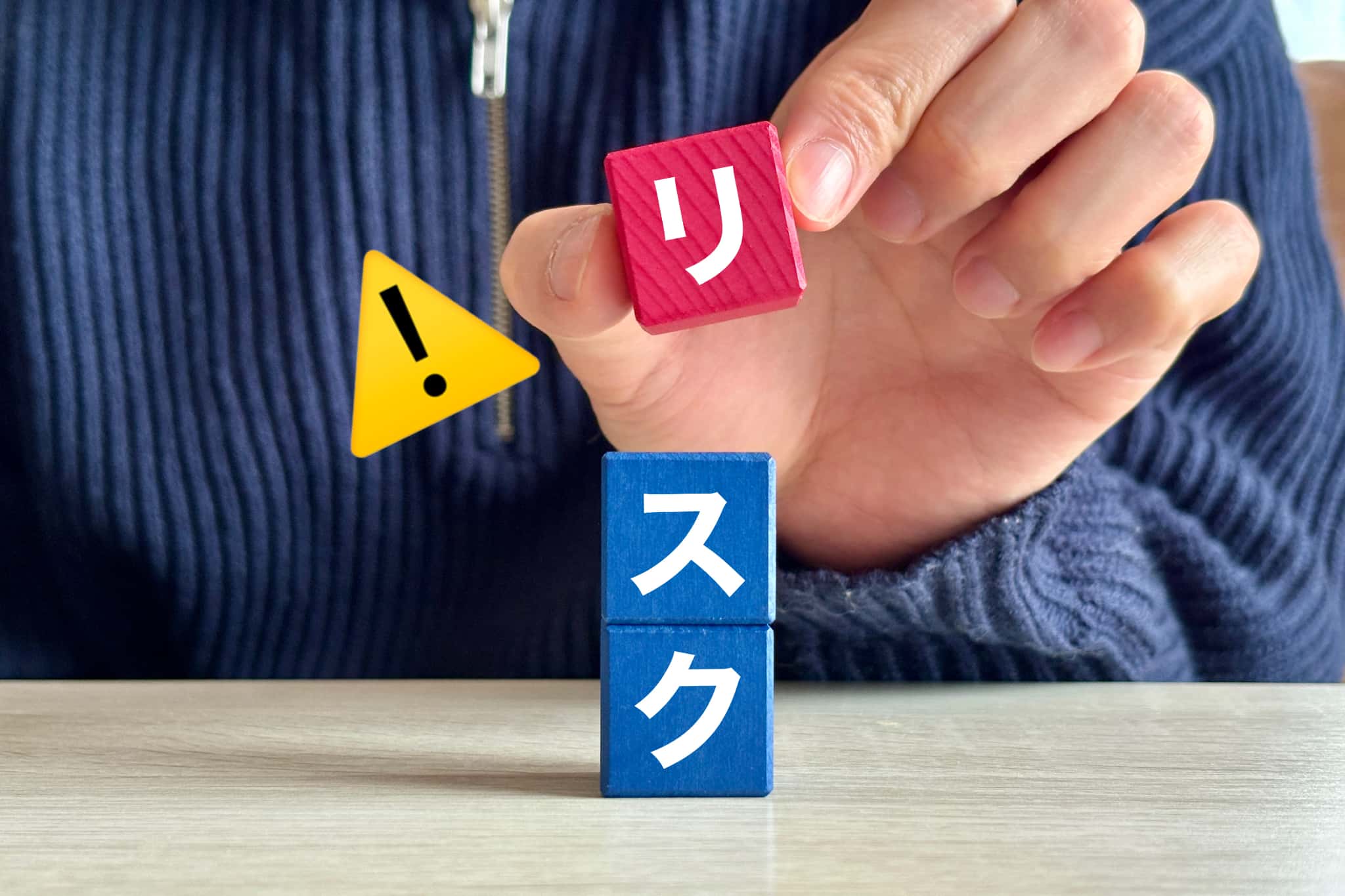 積み木を積んでリスクの文字を作っている手とビックリマーク